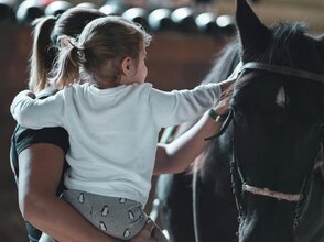 Zdjęcie przedstawia matkę z dzieckiem dotykające konia