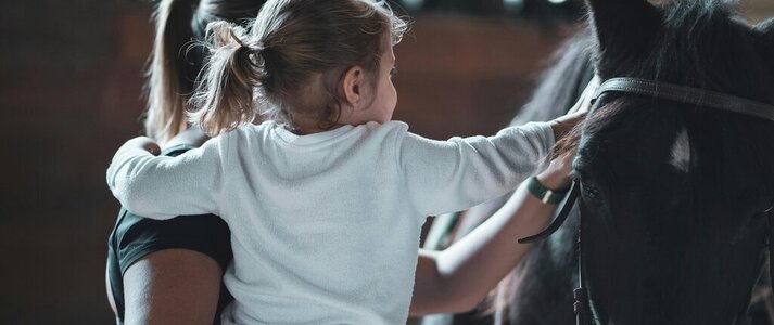 Zdjęcie przedstawia matkę z dzieckiem dotykające konia