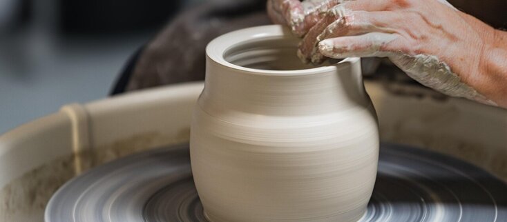 Zdjęcie przedstawia osobę formującą gliniane naczynie na kole garncarskim.