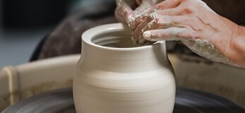 Zdjęcie przedstawia osobę formującą gliniane naczynie na kole garncarskim.