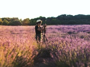 Obrazek przedstawia kobietę na polu lawendy robiącą zdjęcie aparatem pofograficznym na statywnie.