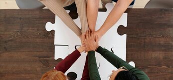 Zdjęcie przedstawia dłonie 4 osób wskazujące na współpracę