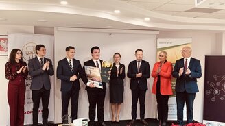 Zdjęcie przedstawia laureata olimpiady wraz z osobami wręczający nagrody