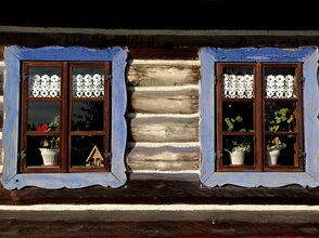 Obrazek przedstawia 2 okna domu drewnianego na wsi.