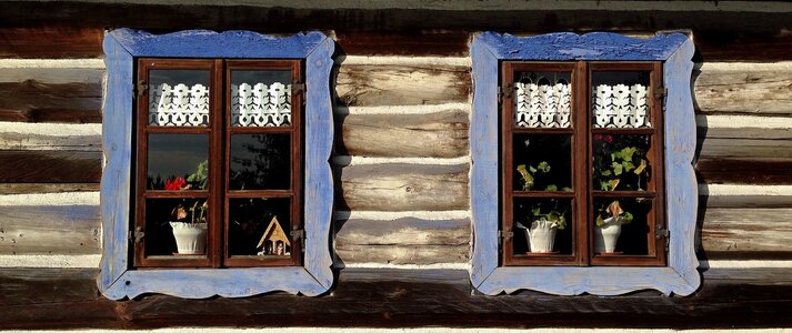 Obrazek przedstawia 2 okna domu drewnianego na wsi.