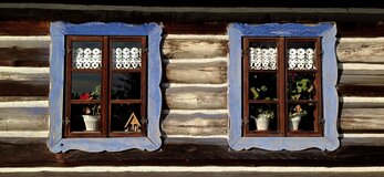 Obrazek przedstawia 2 okna domu drewnianego na wsi.