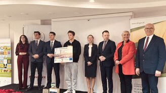 Zdjęcie przedstawia laureata olimpiady wraz z osobami wręczający nagrody