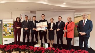 Zdjęcie przedstawia laureata olimpiady wraz z osobami wręczający nagrody