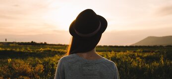 Obrazek przedstawia młodą kobietę patrzącą na pole uprawne