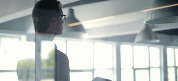 Zdjęcie przedstawia mężczyzną z laptopem, widocznego od tyłu