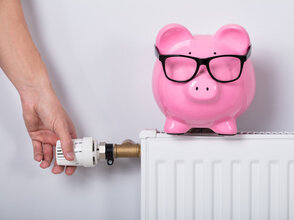 Man's Hand Adjusting Thermostat With Piggy Bank